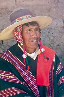 Three people in Aymara attire sitting against a brick wall.