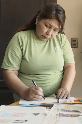 Filmmaker Lourdes Rivas with green shirt writing on a piece of paper with a pen.